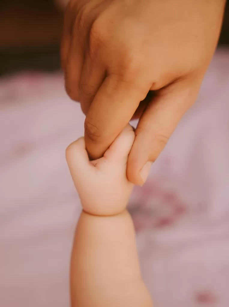 baby holding the finger of their mother